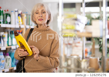 Elderly housewife buys a cleaning product for washing parquet and laminate floors in supermarket 128295276