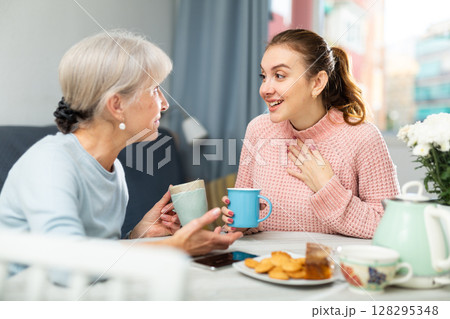 Young woman enjoying conversation with elderly mother over cup of coffee Young woman enjoying conversation with elderly mother over cup of coffee 128295348