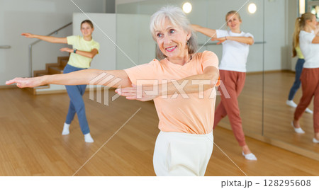 Positive woman doing aerobics exercises with group of people in dance center 128295608