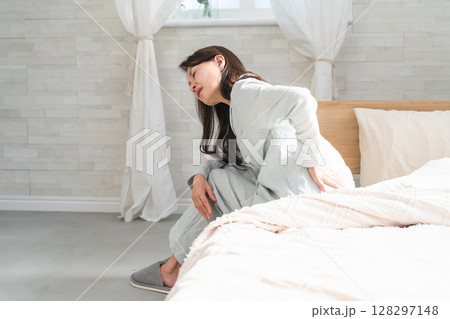 起きてベッドの上で腰痛を訴える女性 起きてベッドの上で腰痛を訴える女性 128297148