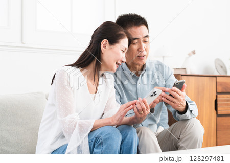 ソファーに座ってスマートフォンを操作している熟年夫婦　ライフスタイルイメージ 128297481
