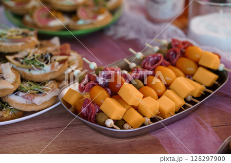 Rustic Charcuterie Board Feast: Salami, Cheese Skewers, Crostini, Tomatoes, Olives and Appetizers on Wood Table, Warm Tones and Party Mood Rustic Charcuterie Board Feast: Salami, Cheese Skewers, Crostini, Tomatoes, Olives and Appetizers on Wood Table, Warm Tones and Party Mood 128297900