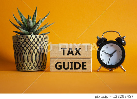 Tax Guide symbol. Concept word Tax Guide on Beautiful orange background with alarm clock and succulent plant. Business and Tax Guide concept. Copy space 128298457