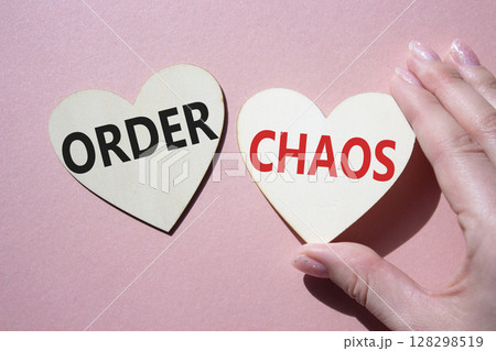 Chaos or Order symbol. Concept word Chaos or Order on wooden hearts. Businessman hand. Beautiful pink background. Business and Chaos or Order concept. Copy space Chaos or Order symbol. Concept word Chaos or Order on wooden hearts. Businessman hand. Beautiful pink background. Business and Chaos or Order concept. Copy space 128298519