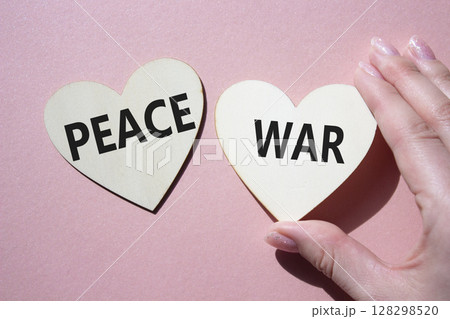 War or Peace symbol. Concept word War or Peace on wooden hearts. Businessman hand. Beautiful pink background. Business and War or Peace concept. Copy space War or Peace symbol. Concept word War or Peace on wooden hearts. Businessman hand. Beautiful pink background. Business and War or Peace concept. Copy space 128298520