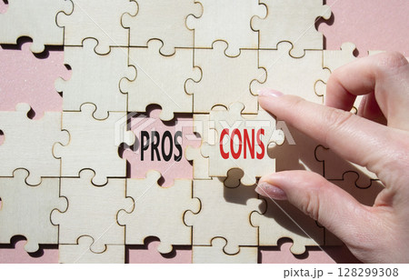 Pros vs Cons symbol. Concept word Pros vs Cons on wooden puzzle. Businessman hand. Beautiful pink background. Business and Pros vs Cons concept. Copy space Pros vs Cons symbol. Concept word Pros vs Cons on wooden puzzle. Businessman hand. Beautiful pink background. Business and Pros vs Cons concept. Copy space 128299308