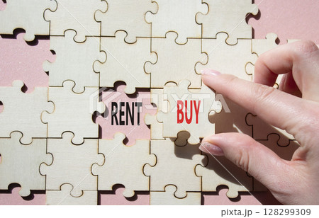 Rent or Buy symbol. Concept word Rent or Buy on wooden puzzle. Businessman hand. Beautiful pink background. Business and Rent or Buy concept. Copy space Rent or Buy symbol. Concept word Rent or Buy on wooden puzzle. Businessman hand. Beautiful pink background. Business and Rent or Buy concept. Copy space 128299309