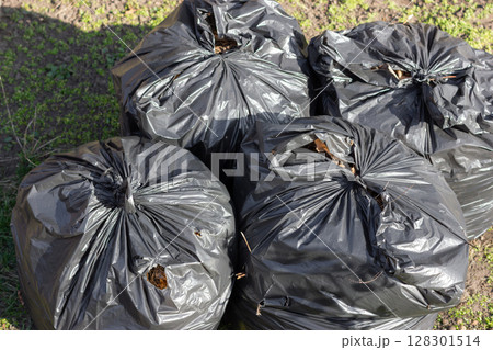 Four black garbage bags on the ground outdoors. Four black garbage bags on the ground outdoors. 128301514