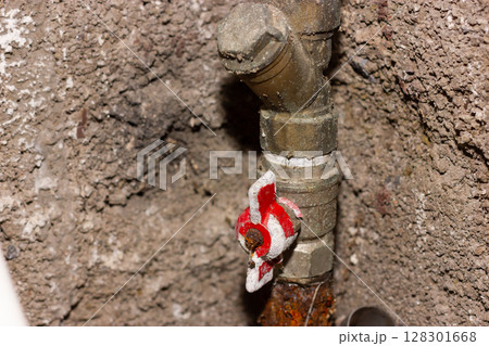 Close-up of an old, rusty pipe valve on a textured wall. 128301668