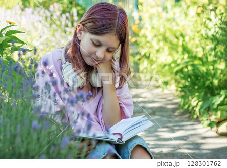 Young student reading a book while listening to music in a garden Young student reading a book while listening to music in a garden 128301762
