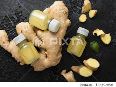 Bottles of immune ginger energy shot drink with ginger roots on black background.Macro. Bottles of immune ginger energy shot drink with ginger roots on black background.Macro. 128302696