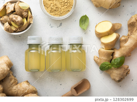 Immune ginger energy shot drink bottles with fresh raw ginger root and powder on light background. Immune ginger energy shot drink bottles with fresh raw ginger root and powder on light background. 128302699