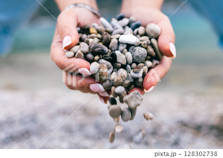 Hands Holding and Releasing Small Pebbles on the Beach Close-Up with Soft Natural Background 128302738