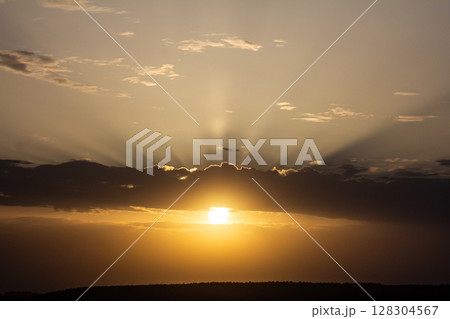 Sunrise casts radiant rays through clouds illuminating the horizon above a tranquil landscape at dawn in the early morning hours Sunrise casts radiant rays through clouds illuminating the horizon above a tranquil landscape at dawn in the early morning hours 128304567