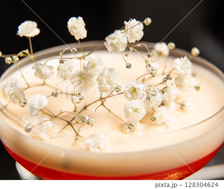 blush-toned cocktail with a frothy top is elegantly garnished with delicate white baby's breath flowers, presented on a golden tray alongside a vintage-style perfume atomizer blush-toned cocktail with a frothy top is elegantly garnished with delicate white baby's breath flowers, presented on a golden tray alongside a vintage-style perfume atomizer 128304624