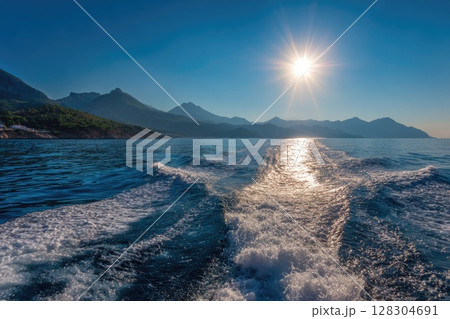 Realistic photo of the sea surface with a blue color and smooth waves, with the sun rising Realistic photo of the sea surface with a blue color and smooth waves, with the sun rising 128304691