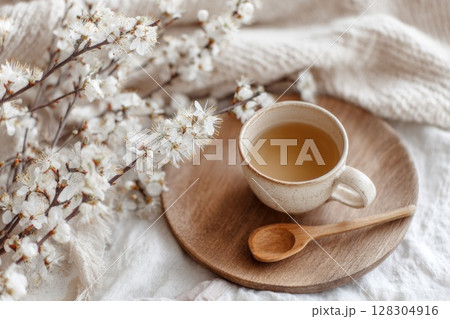 Cup of tea on a wooden plate, with a wooden spoon and white flowers in bloom Cup of tea on a wooden plate, with a wooden spoon and white flowers in bloom 128304916