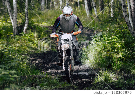 Enduro rider on bike speeding through forest trail during an off-road race 128305979