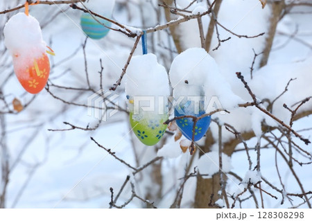 A tree with eggs hanging from it in the snow 128308298