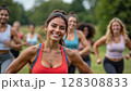 A group of people running in a green park, with a smiling woman in the foreground wearing a red sports bra. - Generic AI Image 128308833