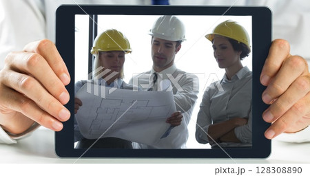 Hands holding digital tablet showing architect discussing plans over blueprint 128308890