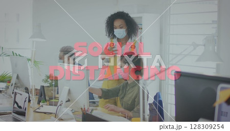 Image of words social distancing with colleagues in office wearing face masks 128309254