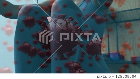 Covid-19 cells floating against woman wearing face mask performing rowing exercise at gym 128309304