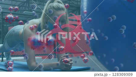 Biohazard symbol and covid-19 cells against woman wearing face mask performing plank exercise at gym Biohazard symbol and covid-19 cells against woman wearing face mask performing plank exercise at gym 128309309