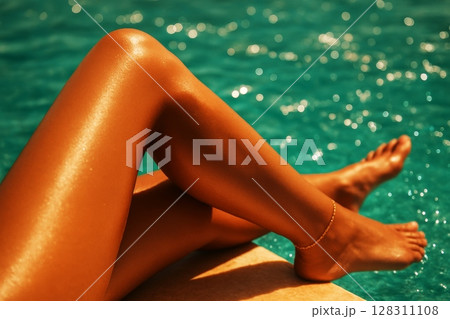 Tanned female legs with anklet resting by turquoise water, summer relaxation and poolside vacation concept, close-up 128311108