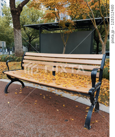 Vibrant autumn leaves cover a park bench in a tranquil urban setting during mid-morning hours 128312480