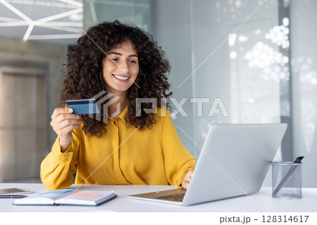Smiling woman holding credit card using laptop for online shopping or financial transactions. Professional atmosphere in modern office setting, conveying ease and convenience of digital banking Smiling woman holding credit card using laptop for online shopping or financial transactions. Professional atmosphere in modern office setting, conveying ease and convenience of digital banking 128314617