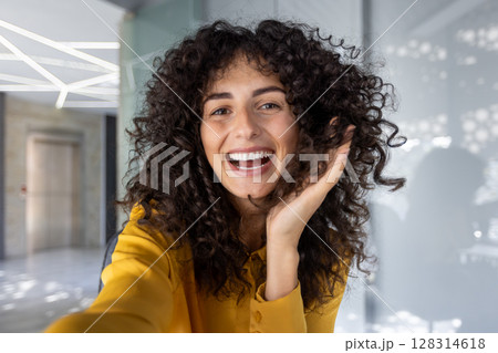 Joyful woman happily smiles during phone video call in office environment. Positive emotion captured as she connects with others through technology, emphasizing friendly communication and interaction Joyful woman happily smiles during phone video call in office environment. Positive emotion captured as she connects with others through technology, emphasizing friendly communication and interaction 128314618