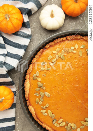 Delicious pumpkin pie with mini pumpkin on grey concrete background. Thanksgiving and fall-themed culinary concept. Delicious pumpkin pie with mini pumpkin on grey concrete background. Thanksgiving and fall-themed culinary concept. 128315564