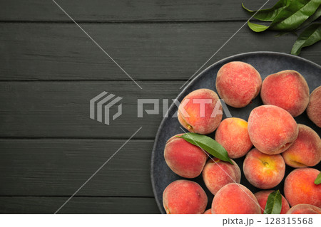 Sweet peaches and leaves on dark plate on black wooden background. Space for text Sweet peaches and leaves on dark plate on black wooden background. Space for text 128315568