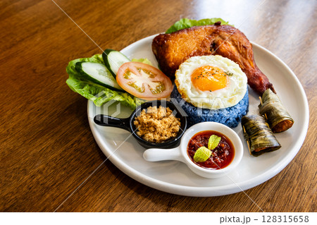 Nasi kerabu, popular delicacy in Malaysia with rice dyed in blue color, served with fried chicken, eggs, kerisik, vergetable and sauces 128315658