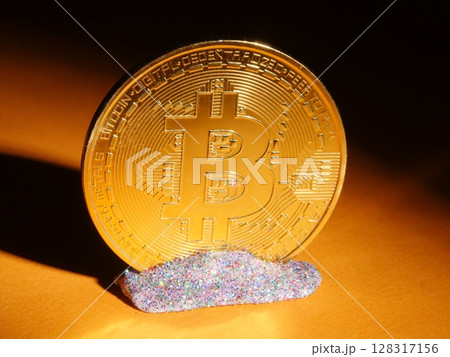 A gold coin with the letter B on it is sitting on a pile of glitter 128317156