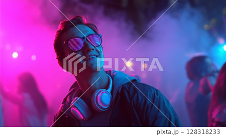 Young man enjoying a vibrant party atmosphere with colorful lights and music in the background during an evening gathering 128318233