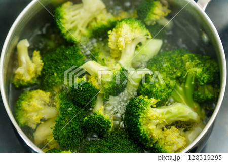 Cooking fresh broccoli in a saucepan over medium heat during a sunny afternoon 128319295