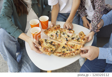 Top view of family members reaching for hot pizza slices, enjoying delicious food together at home. Top view of family members reaching for hot pizza slices, enjoying delicious food together at home. 128320112