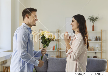 Young man congratulating on holiday his happy girlfriend with bouquet of flowers 128320120