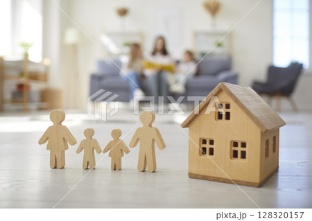 Wooden toy house on floor with figures of people at home with family sitting together in background Wooden toy house on floor with figures of people at home with family sitting together in background 128320157