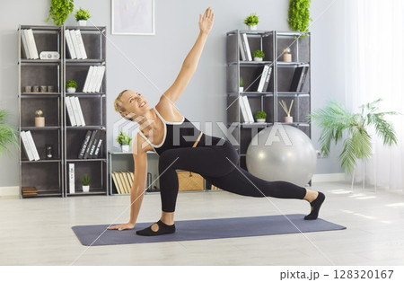 Home yoga workout of girl stretching, athlete standing in Twisted side angle pose on fitness mat Home yoga workout of girl stretching, athlete standing in Twisted side angle pose on fitness mat 128320167