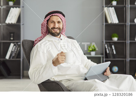 Arabian man having coffee break during doing remote work posing with cup of coffee, digital tablet 128320186