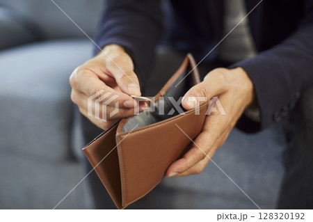 Man sitting on sofa at home wearing suit and putting coin into empty wallet. 128320192