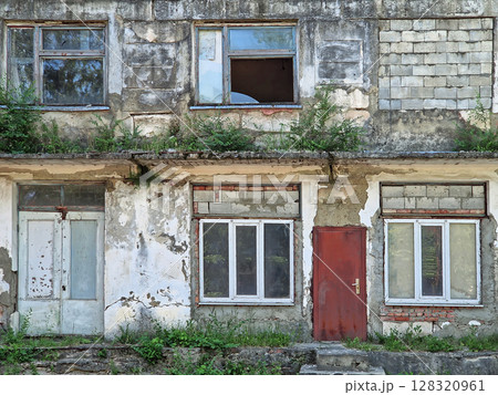 Abandoned building in ruins with peeling paint, crumbling plaster and cracks. Overgrown shrubs and grasses from neglected walls and weathered rafters. Broken windows and exposed bricks reveals decay Abandoned building in ruins with peeling paint, crumbling plaster and cracks. Overgrown shrubs and grasses from neglected walls and weathered rafters. Broken windows and exposed bricks reveals decay 128320961