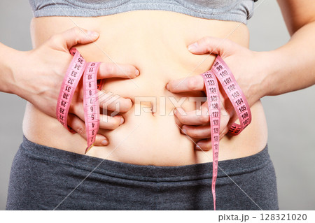 Woman touching stomach holding measuring tape Woman touching stomach holding measuring tape 128321020