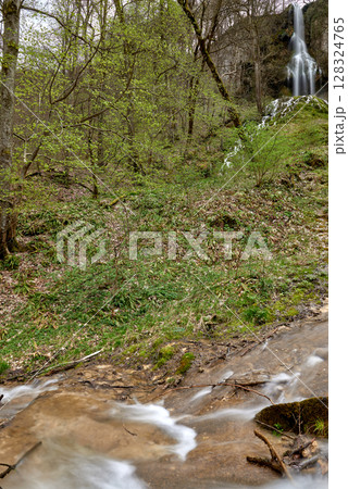 Cascading Waterfall in Lush Forest with Moss-Covered Rocks, Fast-Moving Stream, Wooden Bridge, Serene and Picturesque Atmosphere. 128324765