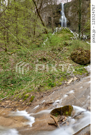 Majestic Forest Waterfall Cascades Through Lush Green Woodland With Hikers Admiring Nature's Beauty From Wooden Bridge. Majestic Forest Waterfall Cascades Through Lush Green Woodland With Hikers Admiring Nature's Beauty From Wooden Bridge. 128324767