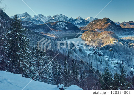 Snowy Mountain Landscape with Iconic Castle Overlooking Serene Lake and Alpine Peaks in Ethereal Winter Wonderland Bathed in Soft Dawn Light Snowy Mountain Landscape with Iconic Castle Overlooking Serene Lake and Alpine Peaks in Ethereal Winter Wonderland Bathed in Soft Dawn Light 128324802
