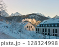 Beautiful alpine architecture in the snow during the golden hour, capturing a serene winter landscape with clear sky and sunny morning light, integrated harmoniously with the mountains. 128324998
